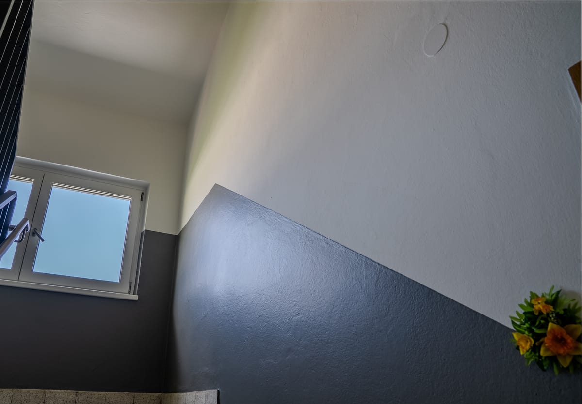 Dasselbe Stiegenhaus nach der Sanierung mit weißer Wand und anthrazitfarbenem Sockel