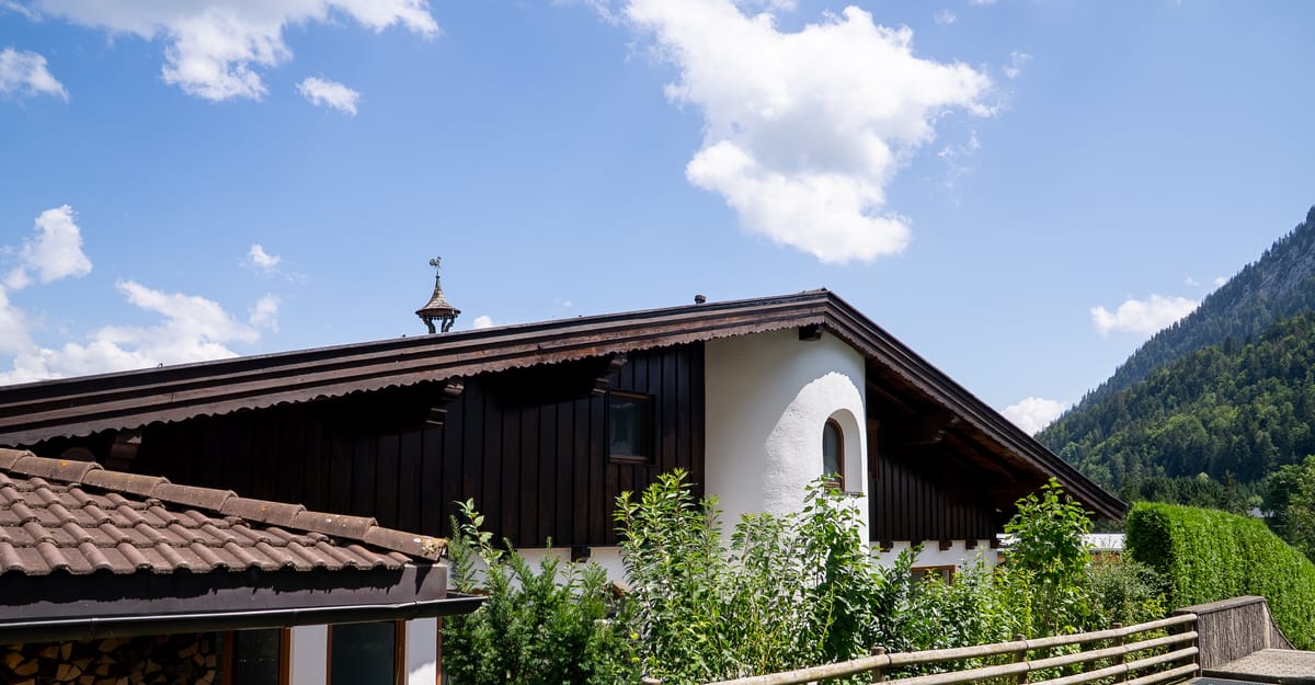 Frisch saniertes Tiroler Landhaus mit weißer Fassade und dunkler Holzverschalung vor Bergkulisse